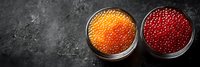 Red and orange caviar in glass bowls on dark stone background, fresh luxury seafood appetizer served as gourmet delicacy. Panoramic food composition.