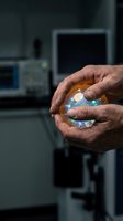 Male scientist or researcher holding illuminated crystal sphere with colorful light refraction in laboratory setting with blurred equipment background, representing innovation, technology, and scientific discovery.