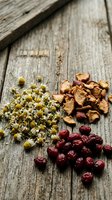 Dried chamomile flowers, rose hips and cranberries arranged on rustic wooden background for herbal tea blending and natural wellness applications.