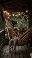Couple relaxing together in striped hammock on wooden porch with hanging lanterns, potted plants and greenery for lifestyle, relationships and outdoor living content.