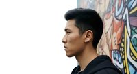 Young Asian male in profile wearing black hoodie against colorful street art graffiti wall background. Urban lifestyle and contemporary culture concept for design projects.