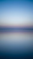 Serene twilight seascape with calm water reflecting pastel sky colors creating peaceful minimalist horizon for meditation and wellness backgrounds.