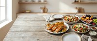 Rustic wooden table set with Mediterranean feast featuring grilled chicken, fresh salads and colorful dishes in bright kitchen setting.
