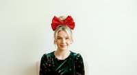 Woman wearing red sequin bow headband and dark green velvet top against neutral background, suitable for holiday portraits, festive fashion, and seasonal marketing campaigns.