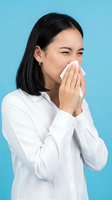 Young Asian woman in white shirt sneezing or blowing nose with tissue against blue background, suitable for healthcare, cold and flu, allergy, wellness and medical content.