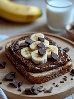 Chocolate hazelnut spread toast topped with fresh banana slices and dark chocolate chunks on wooden plate with milk glass for breakfast or snack.