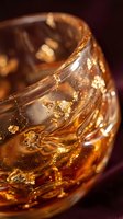 Luxury whiskey glass with swirling amber liquid and shimmering gold flakes, close-up macro shot on dark burgundy background for premium drink concepts.