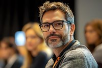 Confident middle-aged Caucasian businessman with glasses and beard smiling at camera during corporate conference or business meeting event.