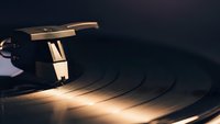Vintage turntable with golden tonearm and stylus on black vinyl record in warm atmospheric lighting for music production and audio entertainment.