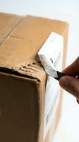 Person with dark skin tone removing white shipping label from cardboard box during unboxing or package inspection process.