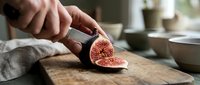 Unrecognizable person slicing fresh figs on wooden cutting board in kitchen, food preparation and cooking concept for culinary content.
