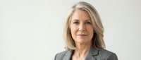 Middle-aged woman with long blonde hair wearing gray blazer against white background, professional headshot for corporate business portrait use.