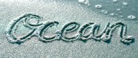 Word Ocean handwritten in wet sand on a sunny beach, with gentle waves nearby, evoking summer travel and coastal relaxation.