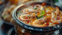 Spicy Asian seafood soup with fresh shrimp, chili peppers and herbs served in traditional hot pot, perfect for restaurant menu, food photography and culinary projects.
