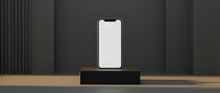 Smartphone with blank white screen displayed on black wooden pedestal against dark gray wall with vertical paneling, suitable for app mockups and tech presentations.