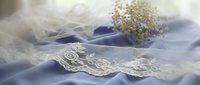Delicate white lace trim with ornate floral embroidery arranged on soft blue and ivory tulle fabric, featuring baby's breath flowers. Perfect for wedding invitations, bridal designs, and formal event materials.