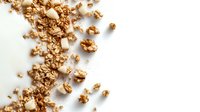 Scattered crunchy granola with nuts and oats on white background, overhead view. Healthy breakfast cereal ingredients in natural golden brown tones.