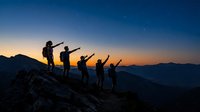 Group of diverse hikers celebrating on mountain summit at sunset, silhouetted against twilight sky with valley below, representing adventure, teamwork and outdoor achievement.