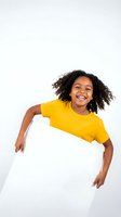 Young woman with curly dark hair and medium skin tone wearing bright yellow t-shirt, smiling while holding blank white sign against neutral background for advertising and promotional campaigns.