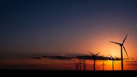 Wind turbines silhouetted against dramatic sunset sky with orange and purple hues. Renewable energy concept for sustainable power generation and clean technology.