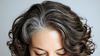 Close-up of woman with natural gray and brown curly hair against neutral background, showcasing aging gracefully for beauty and wellness content.