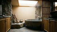 Zen spa bathroom with natural stone walls, wooden soaking tub, bamboo cabinets and skylight creating peaceful wellness retreat atmosphere.