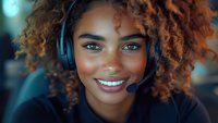 Young African American woman with natural curly hair wearing headset and smiling warmly at camera, professional customer service representative in office setting.