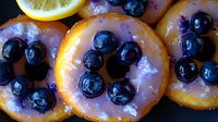 Fresh blueberries arranged on glazed citrus slices with sparkling sugar crystals, creating vibrant contrast of purple and orange for food styling and dessert presentation.