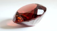 Red faceted garnet gemstone with brilliant cut on white background, showing deep crimson color and natural light reflection. Luxury jewelry element.