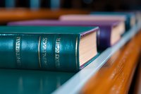 Row of vintage hardcover books on wooden shelf with selective focus on teal blue spine, creating depth of field effect in library or study setting.