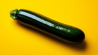 Fresh dark green zucchini on vibrant yellow background with dramatic lighting and shadow creating minimalist food composition for healthy eating concept.