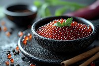 Red caviar served in textured black bowl with soy sauce and fresh herbs, dramatic lighting on dark background creates luxurious gourmet presentation.