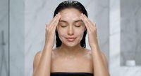 Young Asian woman massaging temples with closed eyes in modern bathroom, stress relief and headache treatment concept for wellness and self-care routine.