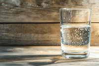Glass of sparkling mineral water with bubbles on rustic wooden table background, refreshing clear beverage in transparent tumbler with copy space.
