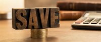 Wooden letter blocks spelling SAVE balanced on stack of coins with calculator in background representing financial planning and money management concepts.