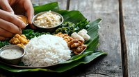 Traditional South Indian meal served on fresh banana leaf with white rice, curry, chutney, and condiments against rustic wooden background.
