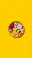 Colorful tropical fruit bowl with dragon fruit, mango, kiwi, papaya and star fruit arranged on bright yellow background for healthy eating concepts.