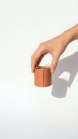 Female hand holding small brown leather cylindrical container against white background with shadow for product photography and design projects.