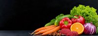 Fresh organic vegetables and fruits arranged on dark background, colorful healthy food composition with carrots, tomatoes, lettuce, citrus and red onion.