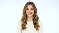 Young woman with long wavy brown hair and fair complexion wearing cream-colored sweater, smiling at camera against white background for portrait and professional use.