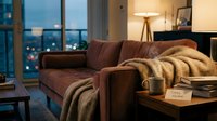 Cozy living room at dusk with a velvet sofa, warm blanket, steaming mug, and stay home note on a wooden coffee table.