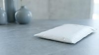 White soft pillow resting on gray surface in minimalist bedroom interior with ceramic vase in blurred background for home decor and comfort concepts.