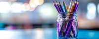 Colorful wooden pencils standing in clear glass mason jar against blurred bokeh background in purple and blue tones. Creative workspace concept.