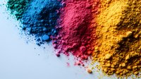 Vibrant powder pigments in blue, pink and yellow scattered on white surface creating colorful gradient border with fine particles and soft texture.