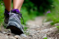 Close-up of hiking boot on rocky mountain trail with blurred green nature background, showing active lifestyle and outdoor adventure sports concept.