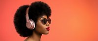Young African American woman with afro hairstyle wearing sunglasses and pink headphones against coral background for music and lifestyle content.