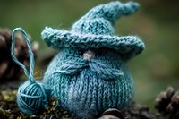 Cozy knitted bunny in soft turquoise wool yarn with pointed ears sitting on moss, accompanied by matching ball of yarn. Handmade toy displays detailed cable knit pattern.