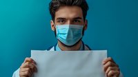 Young male medical professional in protective face mask holding blank white paper against turquoise background, ready for healthcare message or announcement.
