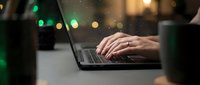 Professional hands typing on laptop keyboard in modern office environment with warm bokeh lights creating productive workspace atmosphere for business technology.