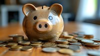 Golden ceramic piggy bank surrounded by scattered coins on wooden table with soft natural lighting, representing savings and financial planning concept.